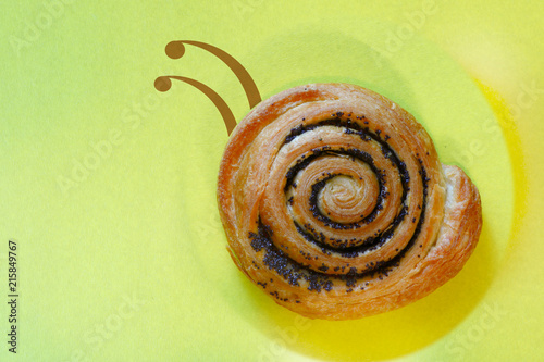 delicious bun with poppy seeds in the form of a snail on yellow background
