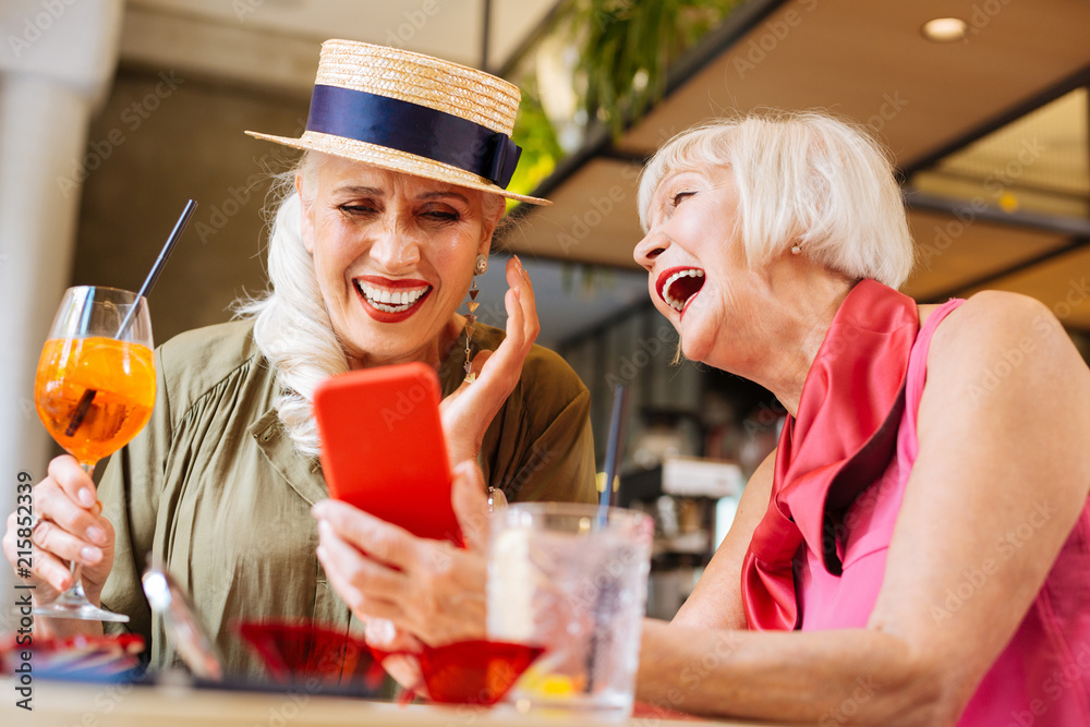 Fototapeta premium New gadget. Positive aged woman smiling while showing her new smartphone to a friend