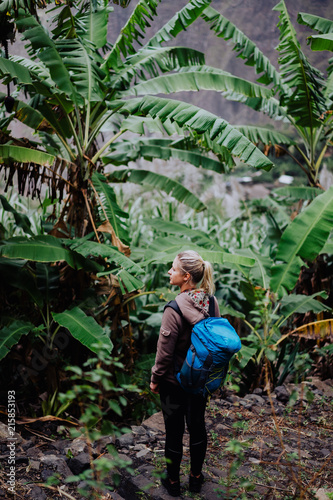 Santo antao island. Cape verde. Blond young women with blue backpack walking through banana plantation on the trekking trail route to Paul valley