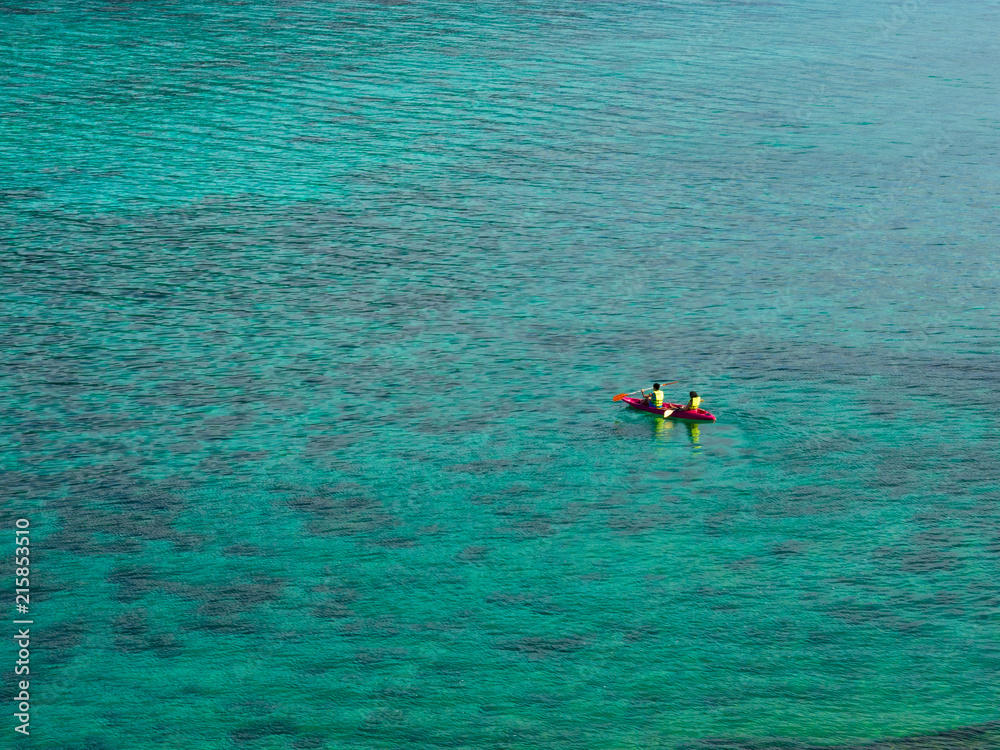 Two travelers in pink  kayak in turquoise water sea for summer vacations holiday concept, bird eye view.