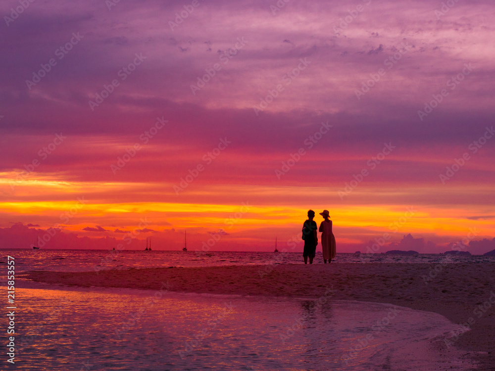 Silhouette of asian couple standing on the beach in sunset time with twilight sky at the sea for romantic honeymoon or vacations holiday concept.