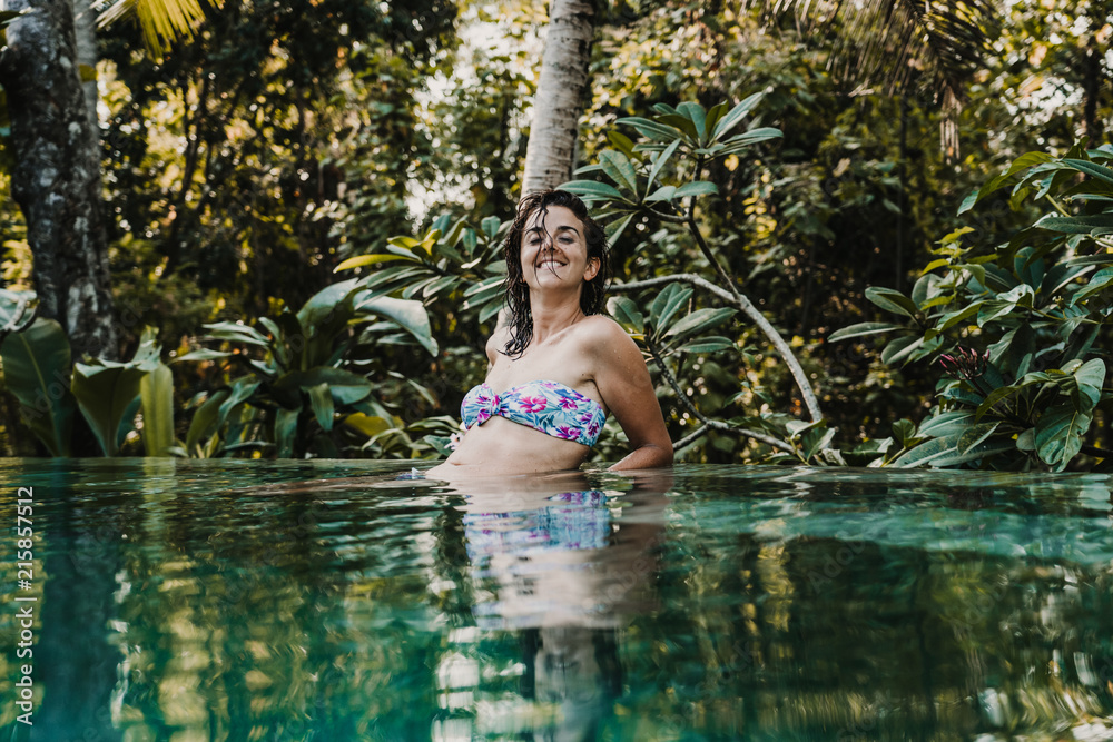 Fototapeta premium .Young and pretty woman enjoying her vacation in Ubud, in the Bali island, Indonesia. A summer afternoon in the pool with a tropical background. Relaxed and happy attitude. Lifestyle.