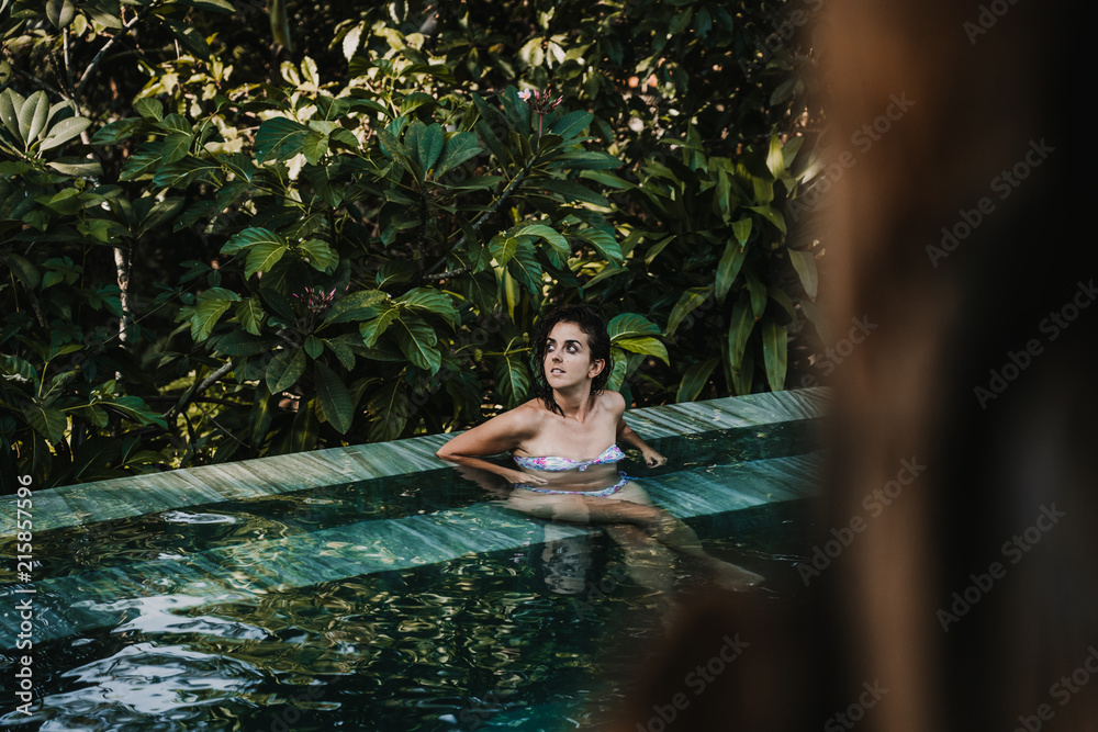 Fototapeta premium .Young and pretty woman enjoying her vacation in Ubud, in the Bali island, Indonesia. A summer afternoon in the pool with a tropical background. Relaxed and happy attitude. Lifestyle.