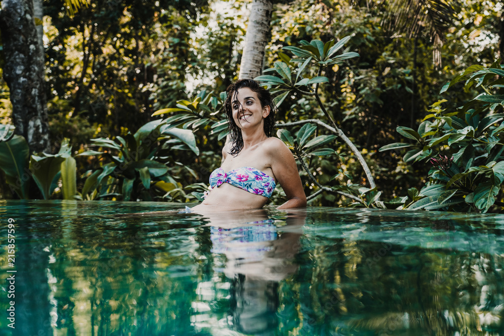 Fototapeta premium .Young and pretty woman enjoying her vacation in Ubud, in the Bali island, Indonesia. A summer afternoon in the pool with a tropical background. Relaxed and happy attitude. Lifestyle.