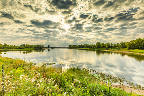 River landscape Millingerwaard at sunrise with overflow basins high water  floodplain forests and blooming wild flowers against blue sky with scattered clouds photo