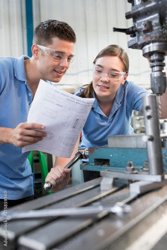 Engineer Instructing Female Apprentice On Use Of Drill Engineer Instructing Female Apprentice On Use Of Drill