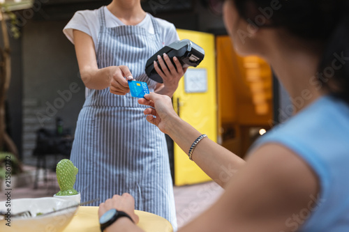 Debit card. Young experienced waitress wearing uniform taking debit card of her constant client