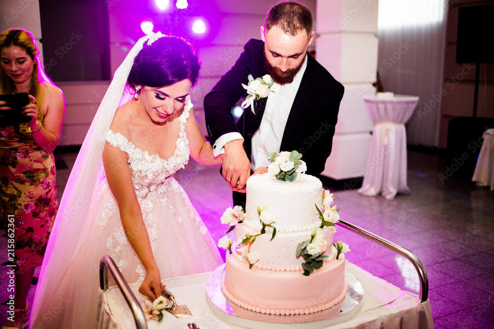 Bride looks happy cutting a wedding cake with a groom Bride looks happy cutting a wedding cake with a groom