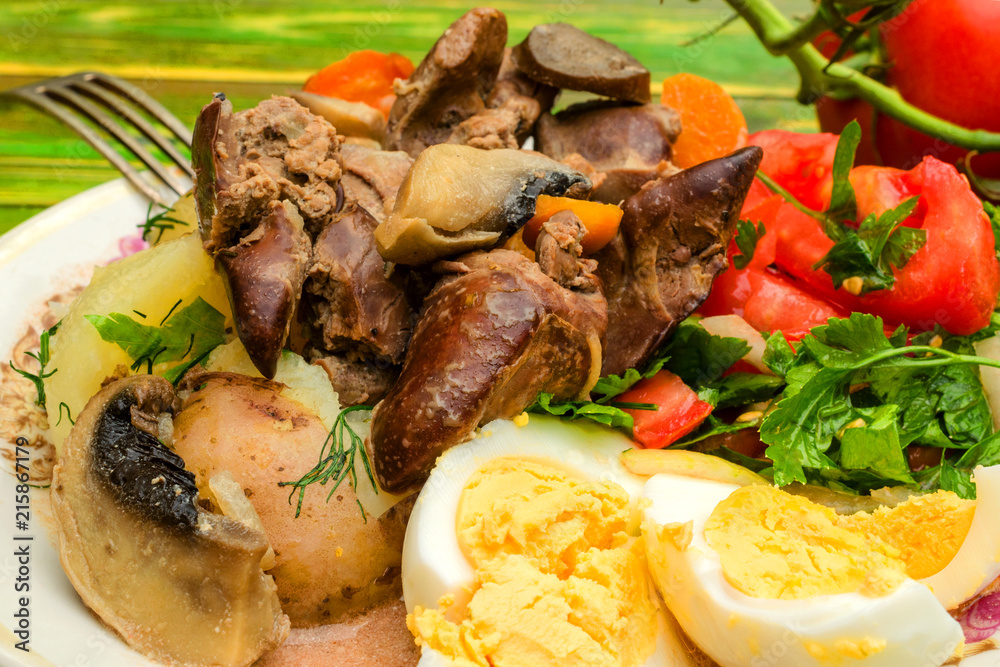 Fried chicken liver, chopped tomatoes with greens and boiled eggs on a white plate. Use for restaurant menu or dish description. The concept of delicious, quality food.
