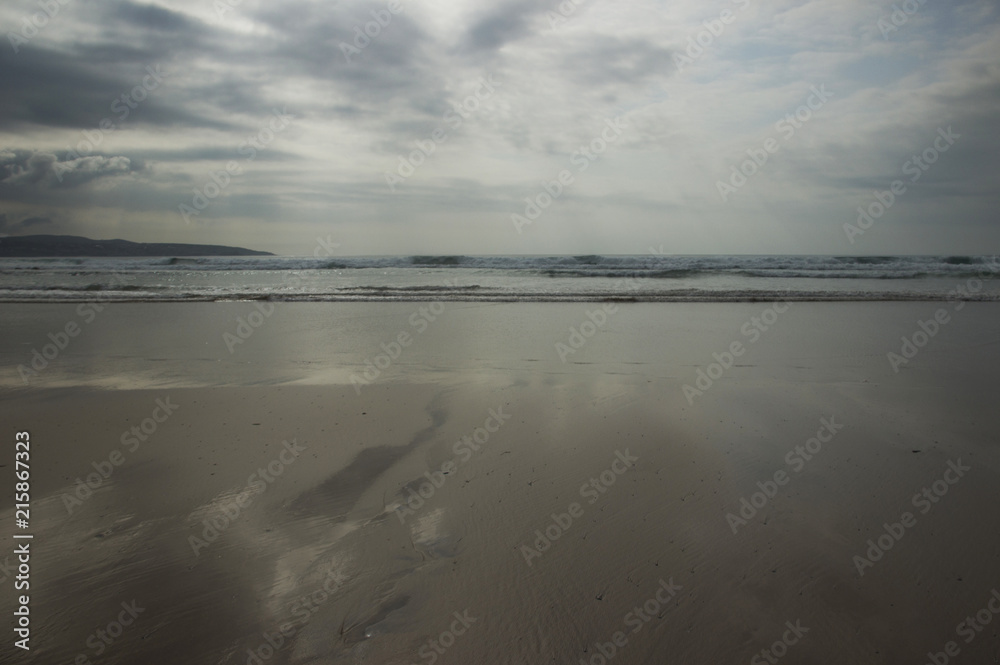 sandy beach and reflections under a grey sky 