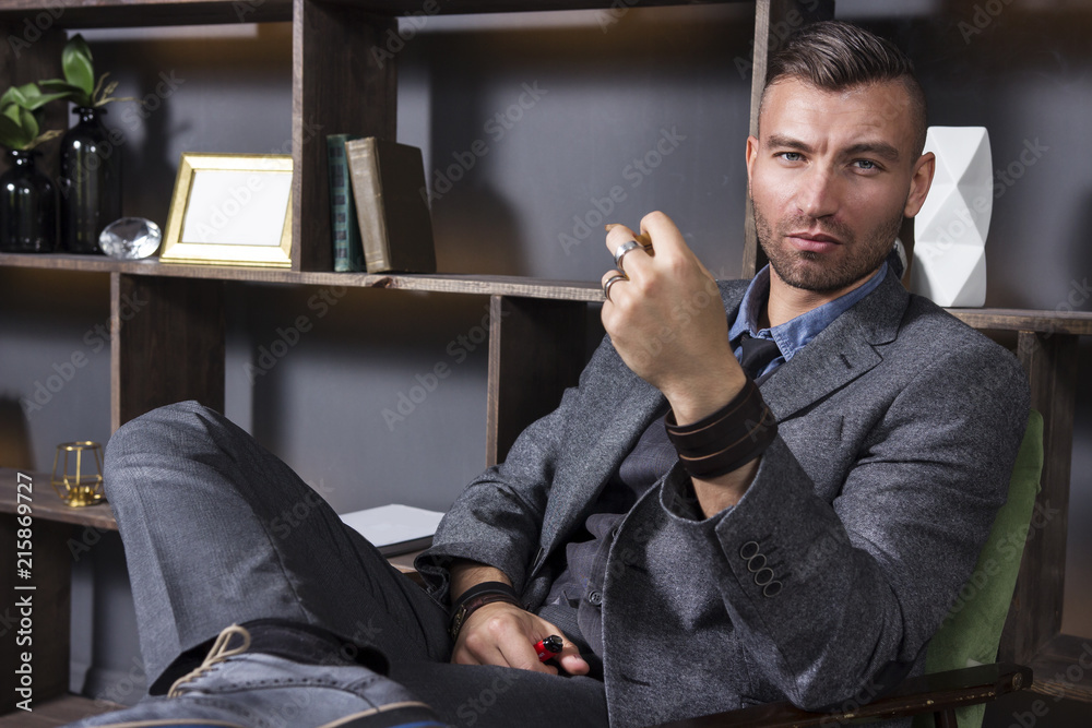 Expressive look of a handsome man in a business suit, who sits in a chair in a luxurious apartment with a smoking pipe.