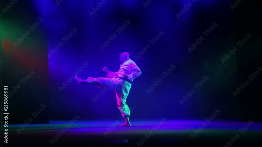 A karate master in a white kimano with a black belt on a black background is engaged in karate A karate master in a white kimano with a black belt on a black background is engaged in karate