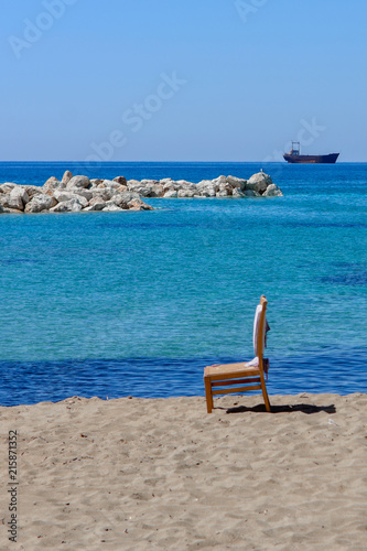 Krzesło stojące na plaży, Morze i kamienie, w tle wrak statku MV Demetrios II, Paphos, Cypr