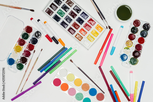 top view of colorful paints, paintbrushes and markers on white table