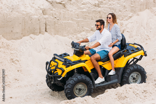 beautiful young couple riding yellow all-terrain vehicle in desert