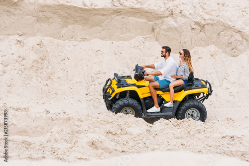 smiling young couple riding all-terrain vehicle in desert