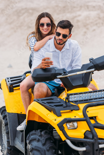 beautiful young couple taking selfie while sitting on ATV in desert