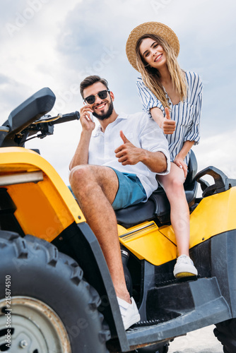 happy young couple sitting on ATV and showing thumbs up