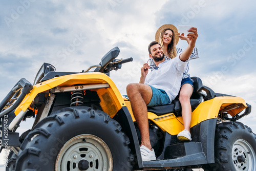 happy young couple sitting on ATV and taking selfie