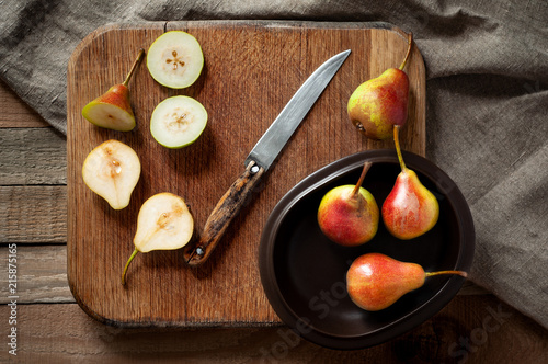 Flat lay of fresh and sliced pears in clay plate with sackcloth on wooden cutting board. Still life in rustic style.