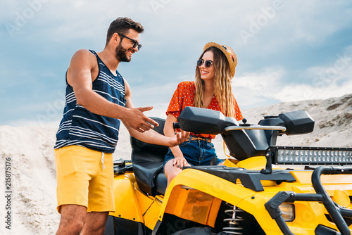 happy young man teaching his girlfriend how to ride atv in desert