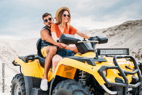 beautiful young couple riding all-terrain vehicle in desert on cloudy day