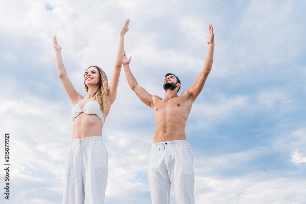 fit young couple with raised arms meditating under cloudy sky fit young couple with raised arms meditating under cloudy sky