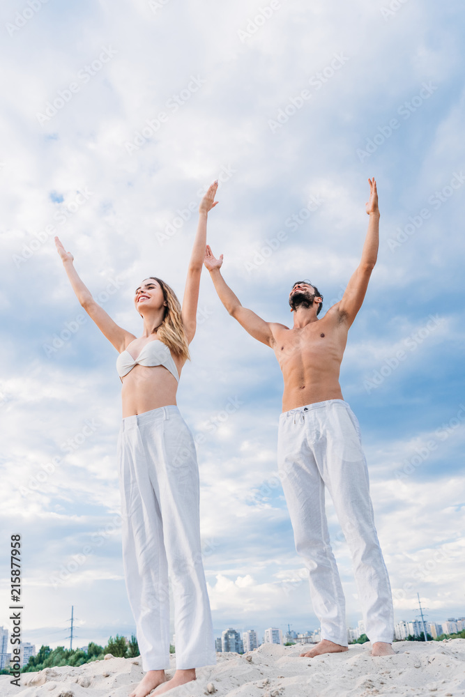 bottom view of fit young couple with raised arms meditating under cloudy sky bottom view of fit young couple with raised arms meditating under cloudy sky