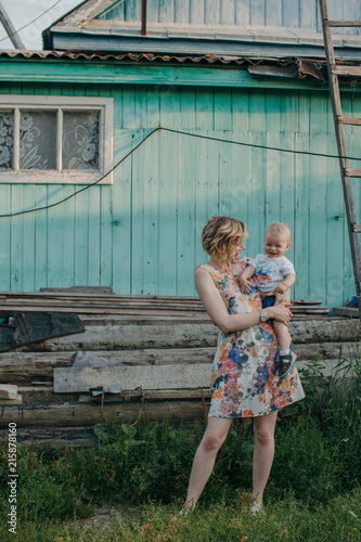 Young pretty mother holding her son on arms in front of bright wall of countryside house photo