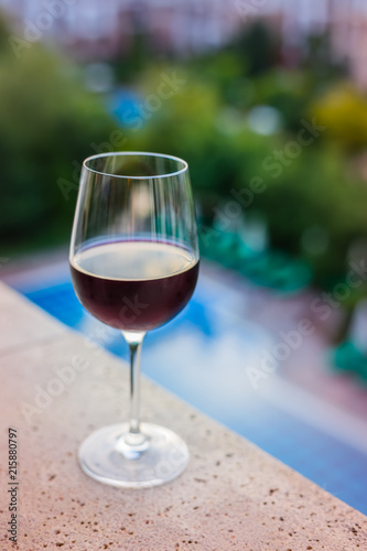 A glass of red wine on the balcony, swimming pool background
