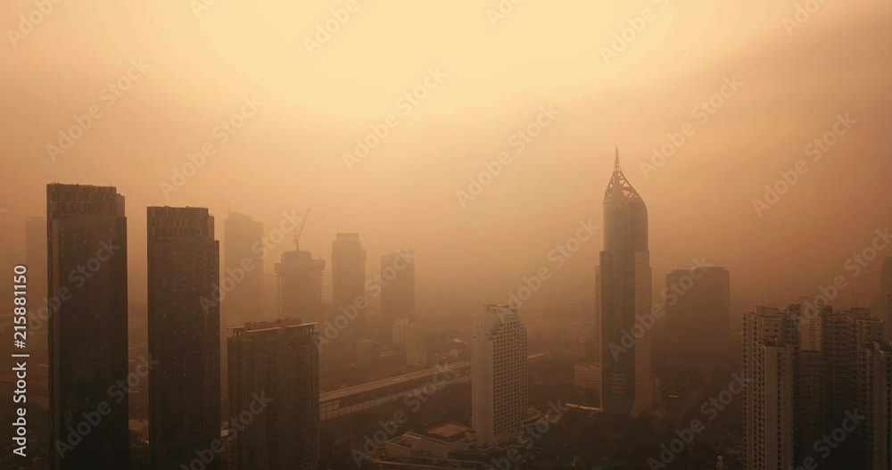 JAKARTA, Indonesia - July 18, 2018: Bird eye view of Jakarta city with smog of air pollution and orange sky at dusk. Shot in 4k resolution