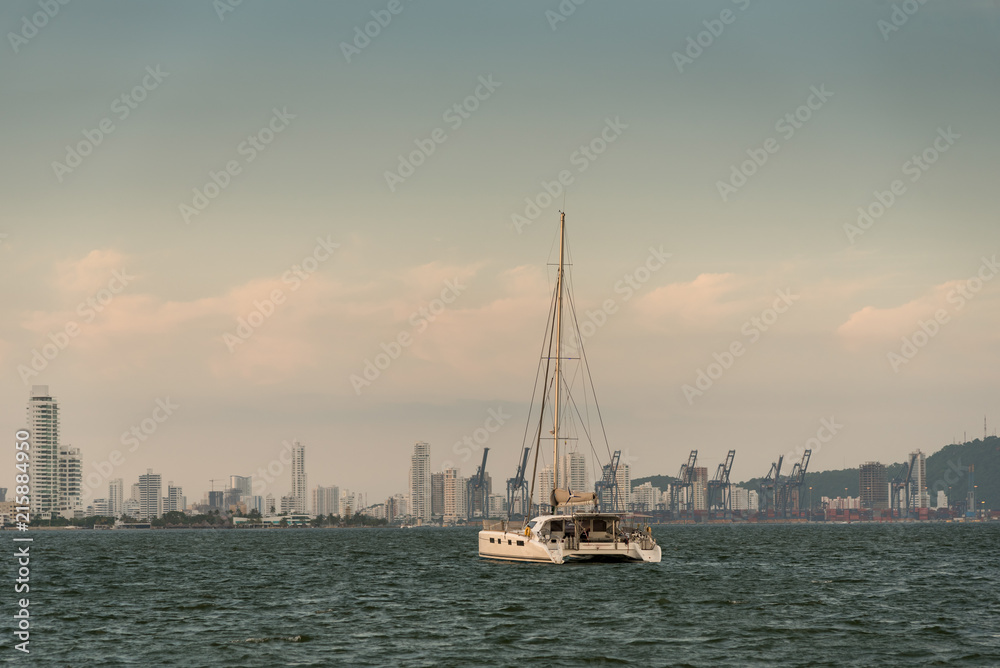 Sailboat boat anchored Cartagena at dusk with commercial port and modern city background. Colombia