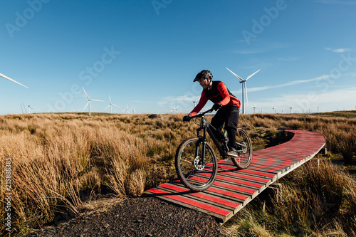 A man in a red and black jersey cycling at speed along a red wooden track at a bike park on a wind farm in Scotland photo