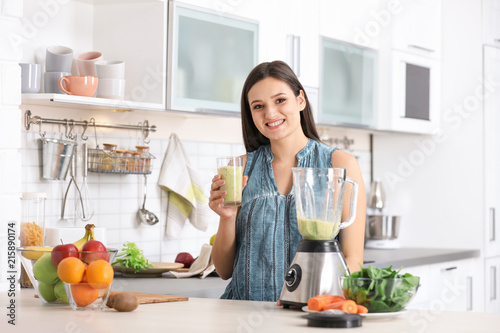 Young woman with tasty healthy smoothie at table in kitchen