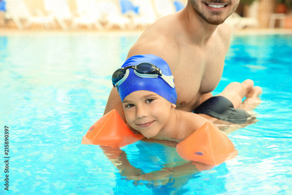 Happy father teaching his son to swim with inflatable sleeves in pool