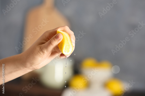 Young woman squeezing lemon on blurred background