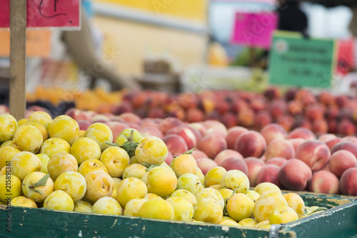 Yellow plum and peaches piled in bins at a farmer's market.  Signage out of focus in the background.