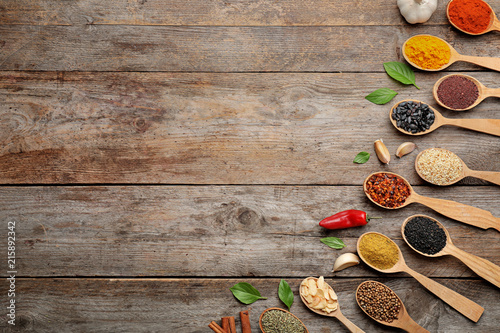 Flat lay composition with different aromatic spices in spoons on wooden background
