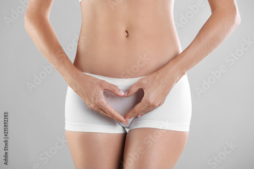 Young woman holding hands in heart shape on grey background. Gynecology concept