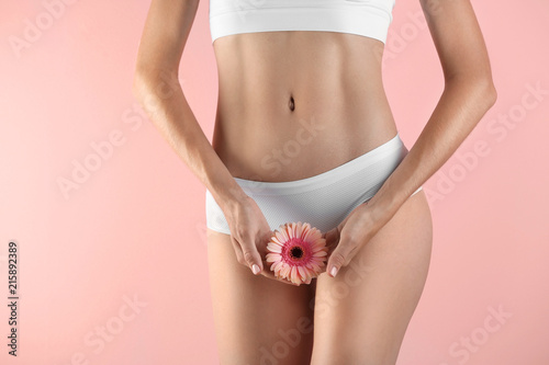 Young woman with gerbera flower on color background. Gynecology concept photo