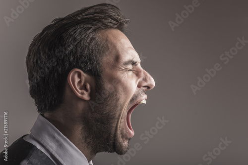 Furious angry young business man shouting and yelling, side view and closeup photo