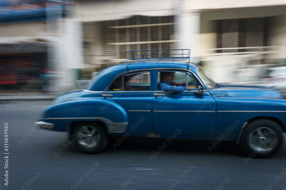 Habana, Cuba - 10 January, 2017:old blue car driving on a cuba street on a beautiful day with some people on the sidewalk