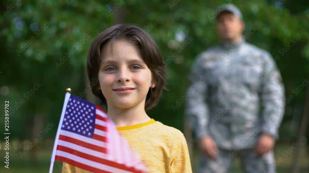 Adorable boy holding american flag, male soldier standing behind, safe future Adorable boy holding american flag, male soldier standing behind, safe future