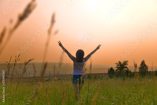 Girl in the field on a sunset background. Woman in the meadow with arms raised.
