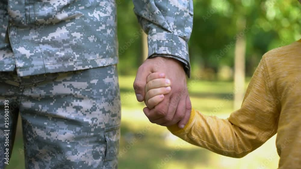 Serviceman holding boys hand, army defending safe future, family togetherness
