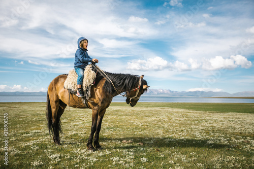 young boy with hoody having fun on a horse on a blooming meadow photo