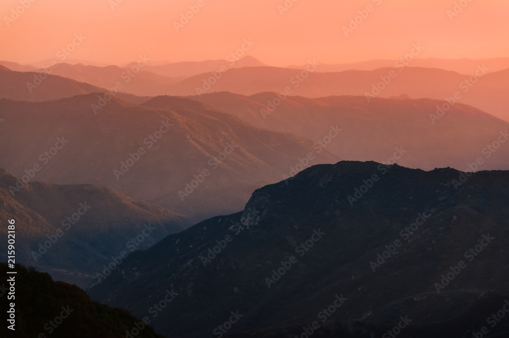 Sunset over mountain ranges of Sierra Nevada in California. Beautiful silhouette with multiple ridge layers and orange haze. Scenic landscape shot from Eleven Range Overlook in Sequoia National Park.