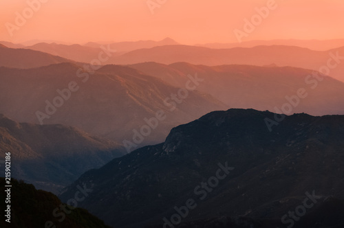 Sunset over mountain ranges of Sierra Nevada in California. Beautiful silhouette with multiple ridge layers and orange haze. Scenic landscape shot from Eleven Range Overlook in Sequoia National Park.