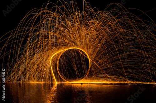 Sparks swirling in a circle above a river, long exposure at night