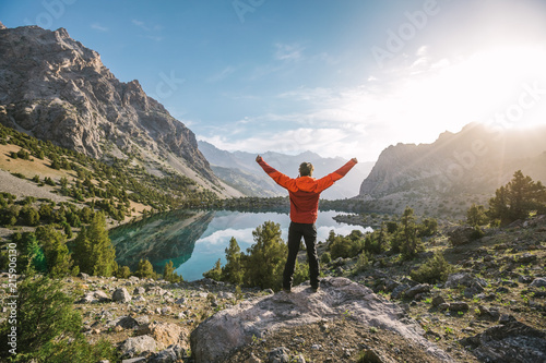 hiker in red jacket raise his hands at a beautiful mountain lake at sunrise photo